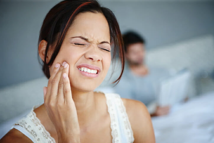 Shot of a woman sitting on the side of her bed with bad toothache